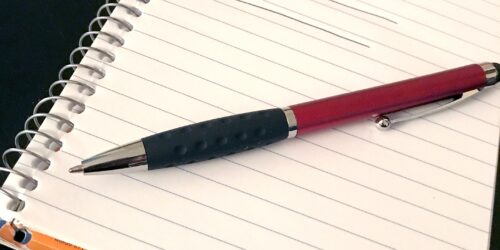 A page from a spiral bound notepad and a pen with the word ' compliance' written on the page